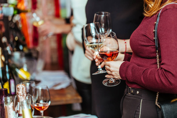  γευσιγνωσία κρασιού: οι επισκέπτες στέκονται κοντά σε τραπέζια με δείγματα γευσιγνωσίας και κρατούν ποτήρια κρασιού. - Φωτογραφία, εικόνα