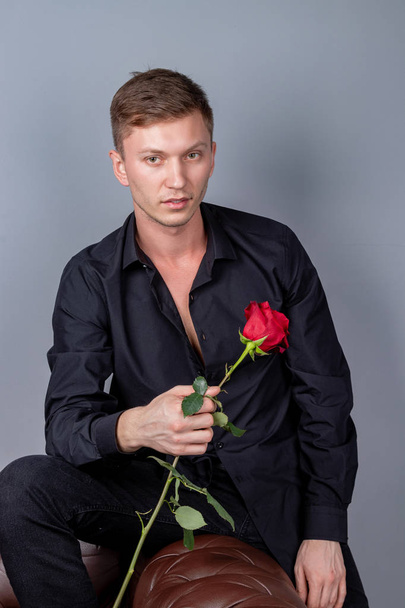 Handsome man wearing black shirt sitting on the leather sofa holding a rose and getting ready romantic date - Φωτογραφία, εικόνα
