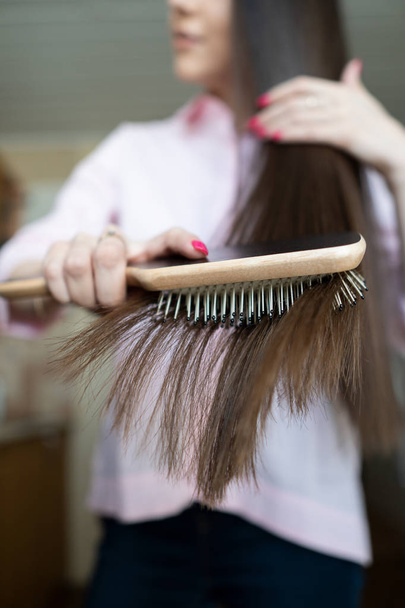 Brunetka dziewczyna w różowej koszulce czesanie jej piękny długi grzebień do włosów - Zdjęcie, obraz