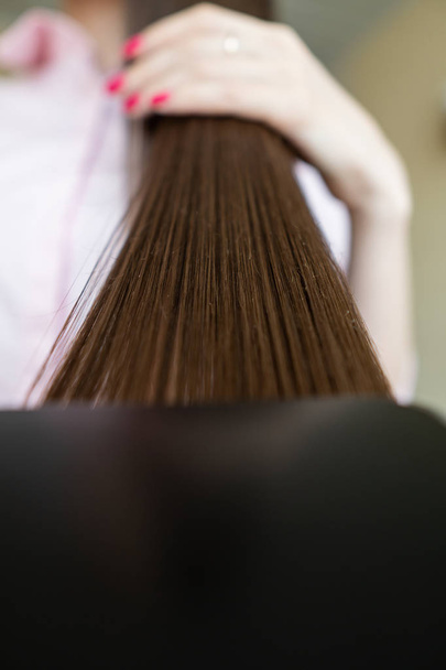 Brunette girl in a pink shirt is combing her beautiful long hair comb - Photo, Image