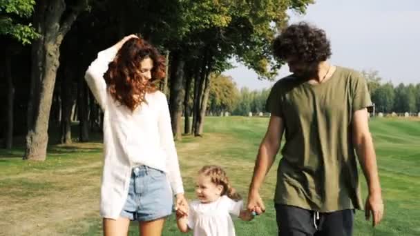 子供を持つ家族は公園の緑の芝生の上を歩きます。ステディカムショット. - 映像、動画
