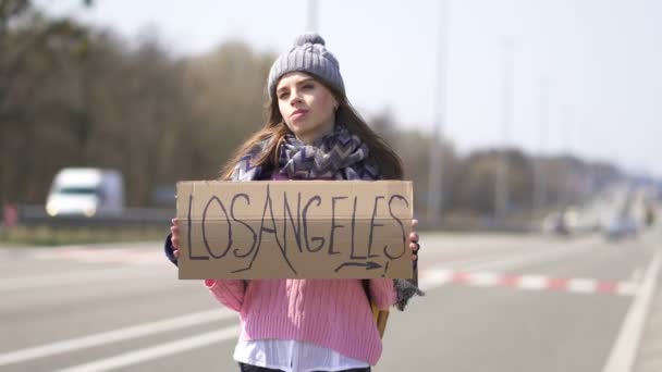 Młoda ładna kobieta autostopem pobyt z plakatem Los Angeles. Zespół podróżny - Materiał filmowy, wideo