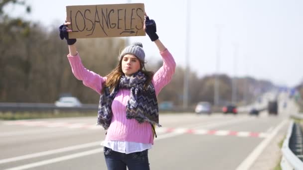 Młoda kobieta autostopem pobyt z plakatem Los Angeles. Zespół podróżny - Materiał filmowy, wideo