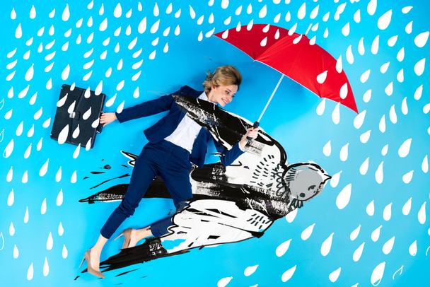 top view of businesswoman in suit with umbrella and briefcase lying on blue background with swallow and rain illustration - Фото, зображення