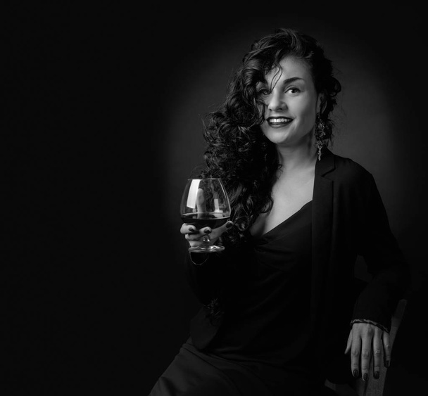 Portrait of attractive brunette with glass of brandy on a black  - Фото, зображення