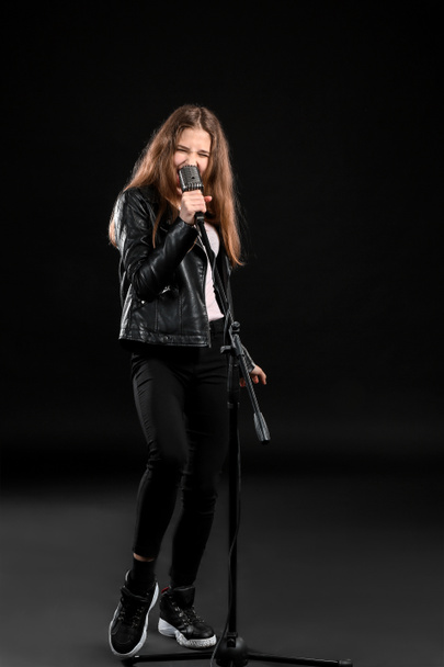 Дівчина-підліток з мікрофоном співає на темному фоні
 - Фото, зображення