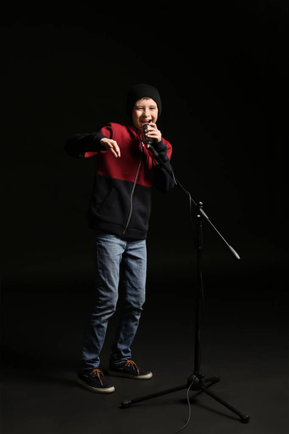 Tiener jongen met microfoon zingen tegen donkere achtergrond - Foto, afbeelding