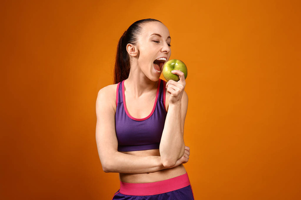 Sportovní žena, která žere jablko na barevném pozadí - Fotografie, Obrázek