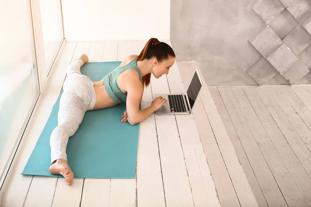 Jeune femme sportive avec ordinateur portable faisant jambe fractionnée dans la salle de gym
 - Photo, image