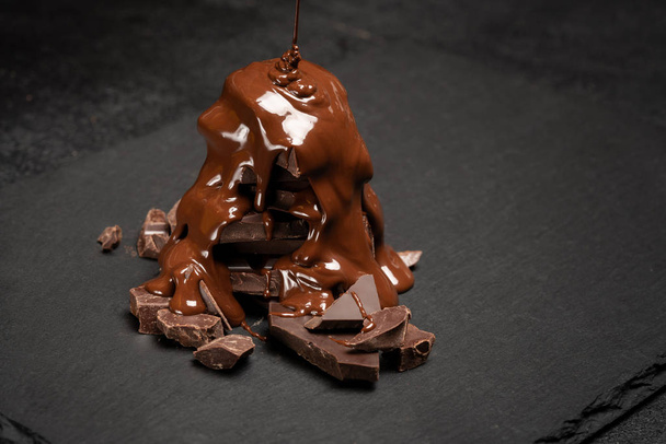 close up of chocolate pieces pile or heap and melted chocolate syrup on dark concrete background - Fotoğraf, Görsel