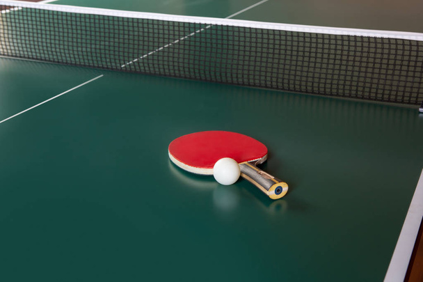 Ping-Pong racket en een bal op een groene tafel. Ping-Pong netto. - Foto, afbeelding