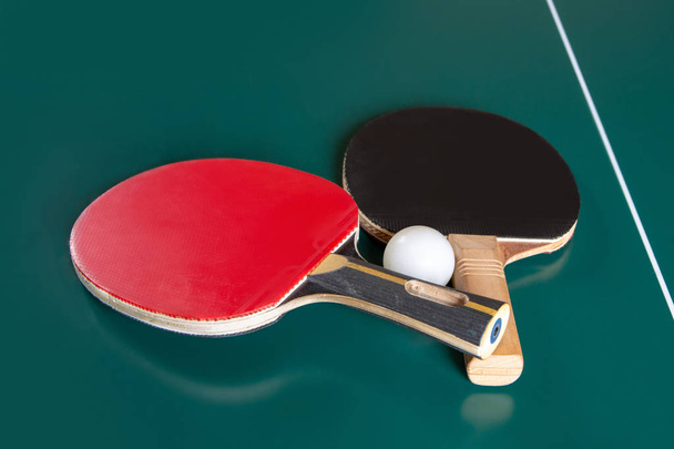 two ping-pong rackets and a ball on a green table.  - Foto, Bild
