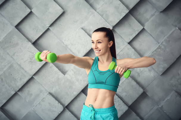 Sporty woman training with dumbbells against grey wall - Фото, изображение