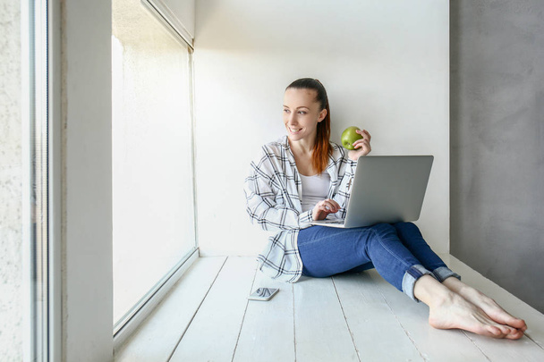 Young woman eating apple while working on laptop indoors - Foto, imagen