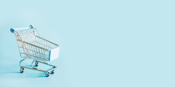 One grocery trolley on pastel blue with space for text. - 写真・画像