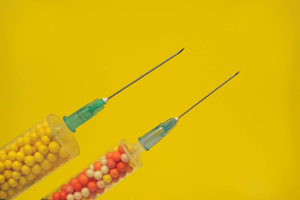 Dwie strzykawki wypełnione kolorowymi nano kulki na żółtym tle. Innowacyjna koncepcja medyczna. Widok makro. - Zdjęcie, obraz