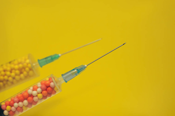 Deux seringues remplies de nano boules colorées sur fond jaune. Concept médical innovant. Vue macro
. - Photo, image