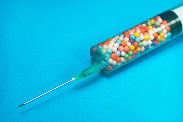 Seringue remplie de nano boules colorées sur fond bleu. Concept médical innovant
.  - Photo, image