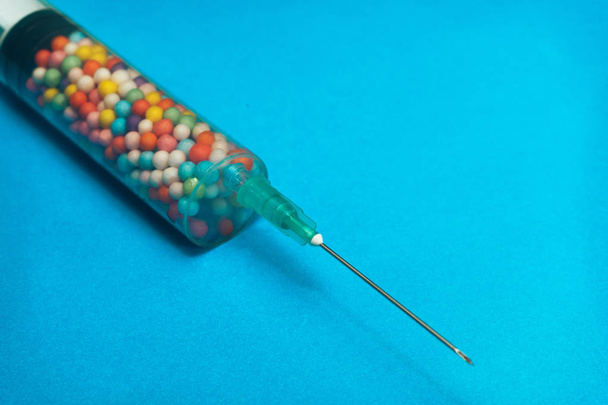 Jeringa llena de nano bolas de colores sobre un fondo azul. Concepto médico innovador
.  - Foto, Imagen