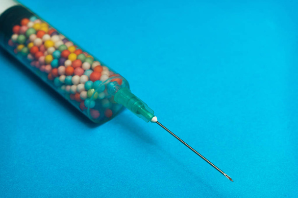 Strzykawka wypełniona kolorowymi nano kulki na niebieskim tle. Innowacyjna koncepcja medyczna.  - Zdjęcie, obraz