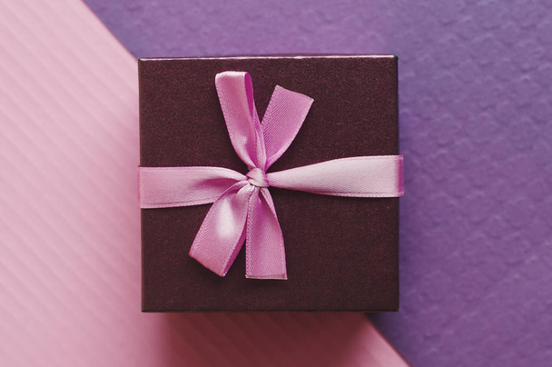 Pequeña caja de regalo con cinta rosa sobre fondo púrpura y rosa, vista superior
 - Foto, imagen