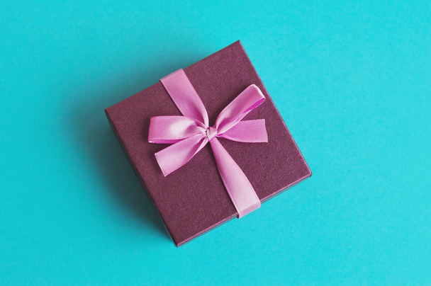 ターコイズの背景にピンクのリボンを持つ小さな紫色のギフトボックス。記念日、誕生日、新年、クリスマスプレゼント - 写真・画像