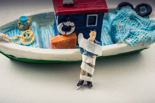 Homem minúsculo em bandagem por um barco modelo
 - Foto, Imagem