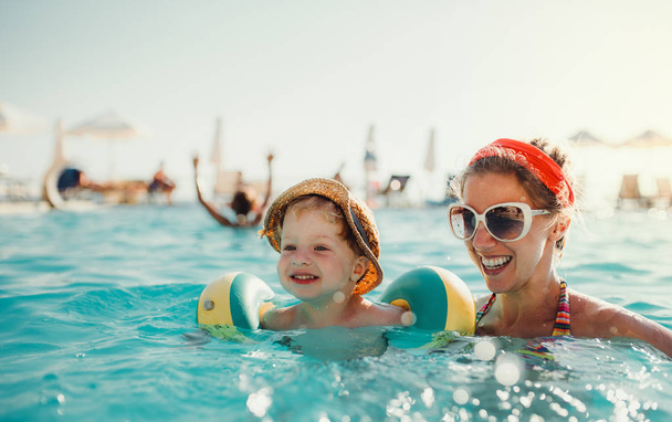 Chłopiec drobny z opaski i matki, pływanie w wodzie na letnie wakacje. - Zdjęcie, obraz