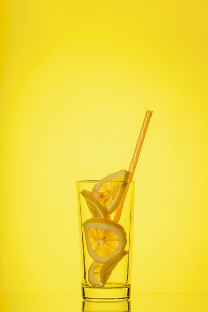 Glass with lemon in sunlight on yellow background - Photo, image