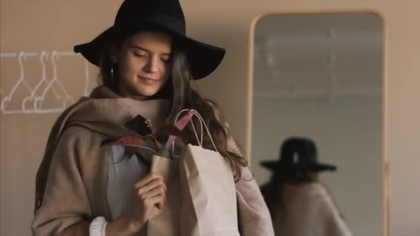 Modne dziewczyny z makiety worek papierowy stwarzające w pomieszczeniu przed zakupami 4K. Młoda kobieta ubrana w stylu boshow patrząc na odbicie lustrzane szczęśliwe emocje. Trendy ekologiczne przemysł mody - Materiał filmowy, wideo