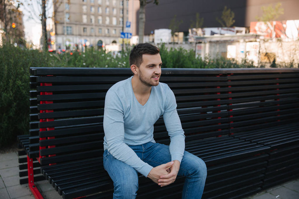 Jóképű ember ül a padon a város központjában. Boldog ember kívül - Fotó, kép