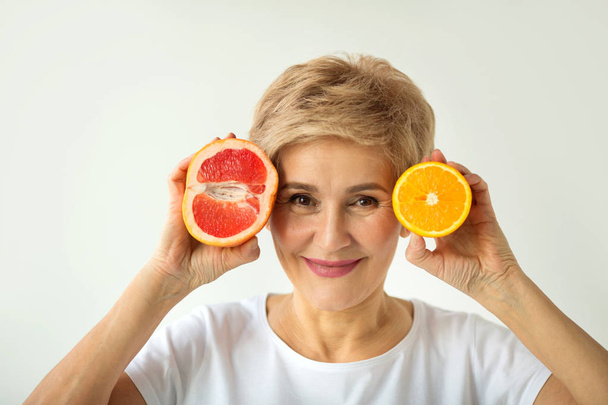 beautiful elderly woman in white t-shirt with orange and grape-fruit in hands on white background - Foto, Imagem