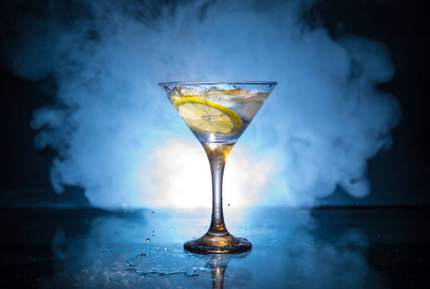 Martini-Cocktailglas auf dunklem, rauchigen Hintergrund oder bunter Cocktail im Glas mit Spritzern und Zitrone. Party Club Unterhaltung. gemischtes Licht. Selektiver Fokus - Foto, Bild