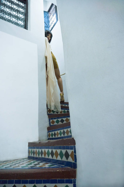 美しいモロッコ少女短い黄金のドレスとマラケシュのリヤド言った美しいダール Si の豊かな内部でホワイト マント マント - 写真・画像