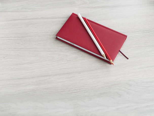 Accesorios de oficina: un bloc de notas rojo, un lápiz blanco y un lápiz rojo sobre un escritorio gris de madera. De vuelta a la escuela. Vista superior. Copiar espacio
 - Foto, Imagen