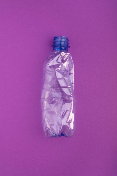 Crashed plastic bottle on blue purple background. Plastic utilisation concept. Ecological problem, global environment. - Photo, image
