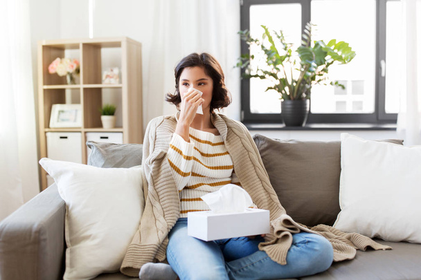 sick woman blowing nose in paper tissue at home - Foto, Imagem