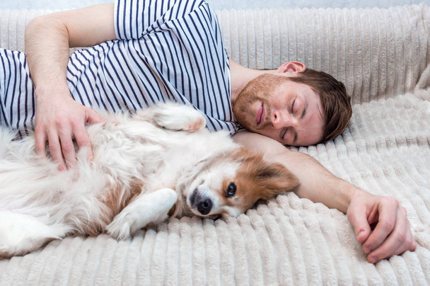 Портрет молодого чоловіка, який спить зі своїм собакою в обіймах на ліжку
 - Фото, зображення