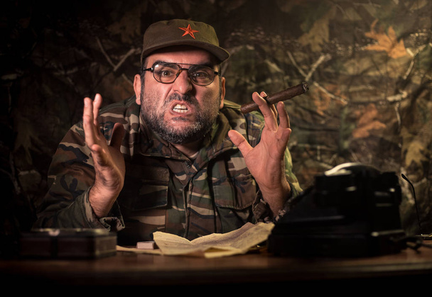 den bösen Diktator, der auf dem Tisch sitzt. wütender kommunistischer General im Hauptquartier oder kubanischer Kommandeur im dunklen Raum. Studiodekoration - Foto, Bild