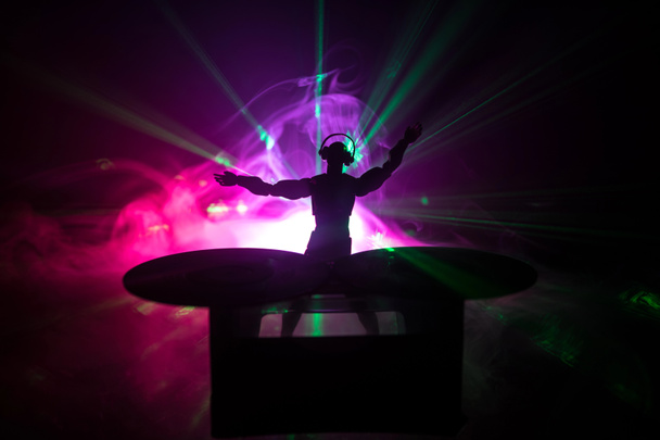 dj club konzept. DJ-Mixing und Kratzen in einem Nachtclub. Männersilhouette auf Vinyl-Plattenspieler, Blitzlicht und Nebel im Hintergrund. Kreative Kunstwerke Dekoration mit Spielzeug. Selektiver Fokus - Foto, Bild
