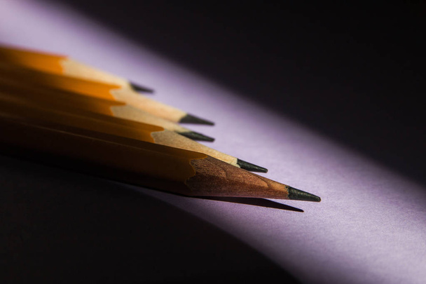 five simple pencils on a solid purple background in hard sunlight contrasting light from the window with a copy space. selective focus - Foto, immagini