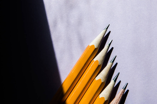 five simple pencils on a solid purple background in hard sunlight contrasting light from the window with a copy space. selective focus - Фото, изображение