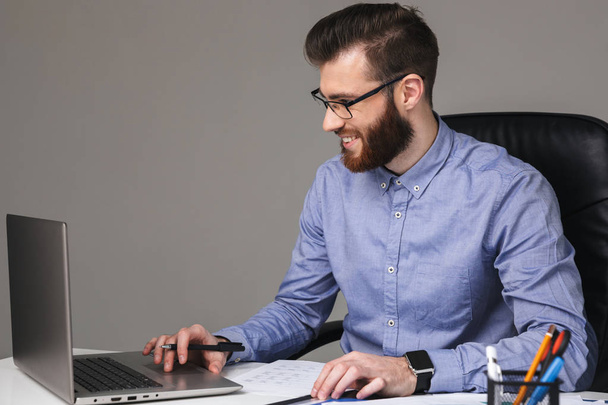 Smiling bearded elegant man in eyeglasses using laptop computer - Fotó, kép