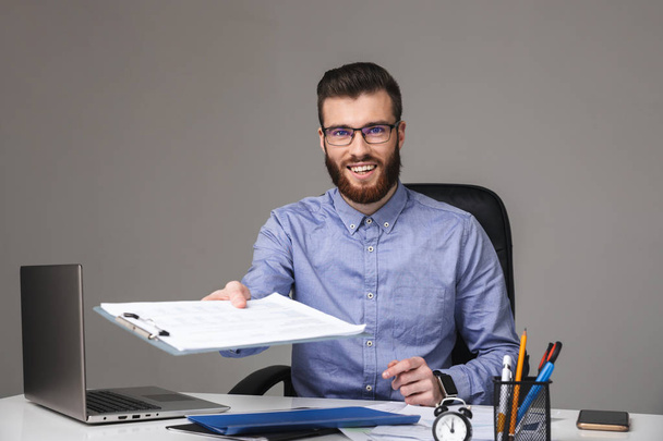 Smiling bearded elegant man in eyeglasses giving clipboard at camera - Foto, afbeelding
