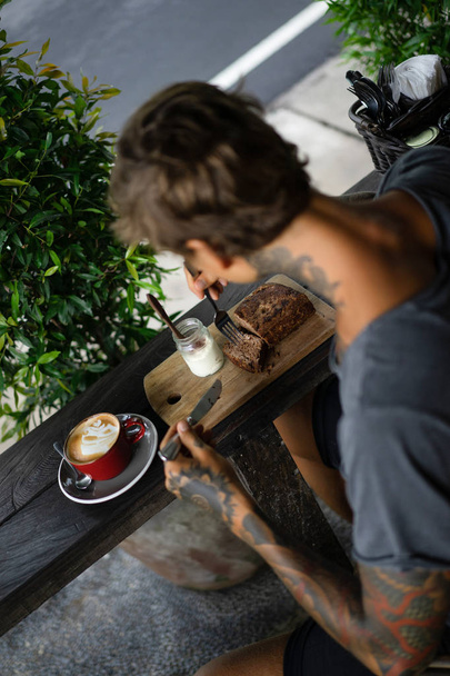 handsome tattooed man having breakfast in a cafe, drinking coffee. man in tattoos - Fotó, kép