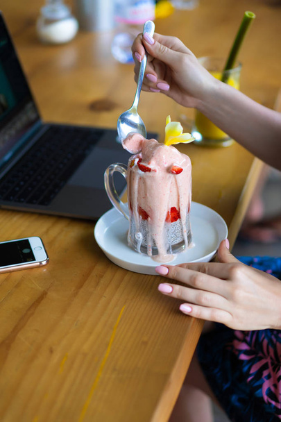 young female working on a laptop, healthy breakfast with chia seeds and juice. Freelance laptop smartphone breakfast. using smartphone and laptop touch screen display - Photo, image