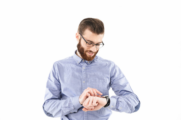 Smiling bearded elegant man in eyeglasses using his wristwatch - Photo, Image