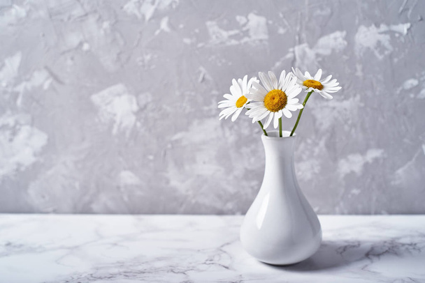 White vase with beautiful chamomile (daisy) flowers isolated on plaster grey wall background, copy space. Home decor - Фото, зображення