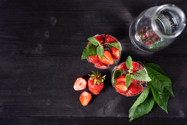 Detox infused water with strawberry and mint in sparkling glasses and bottle on wood table background, copy space. Cold summer drink. Mineral water. Top view, flat lay - Valokuva, kuva