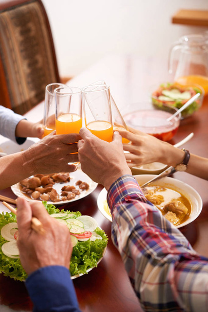 Ręce członków rodziny klinujące kieliszki soku pomarańczowego na stole obiadowym - Zdjęcie, obraz